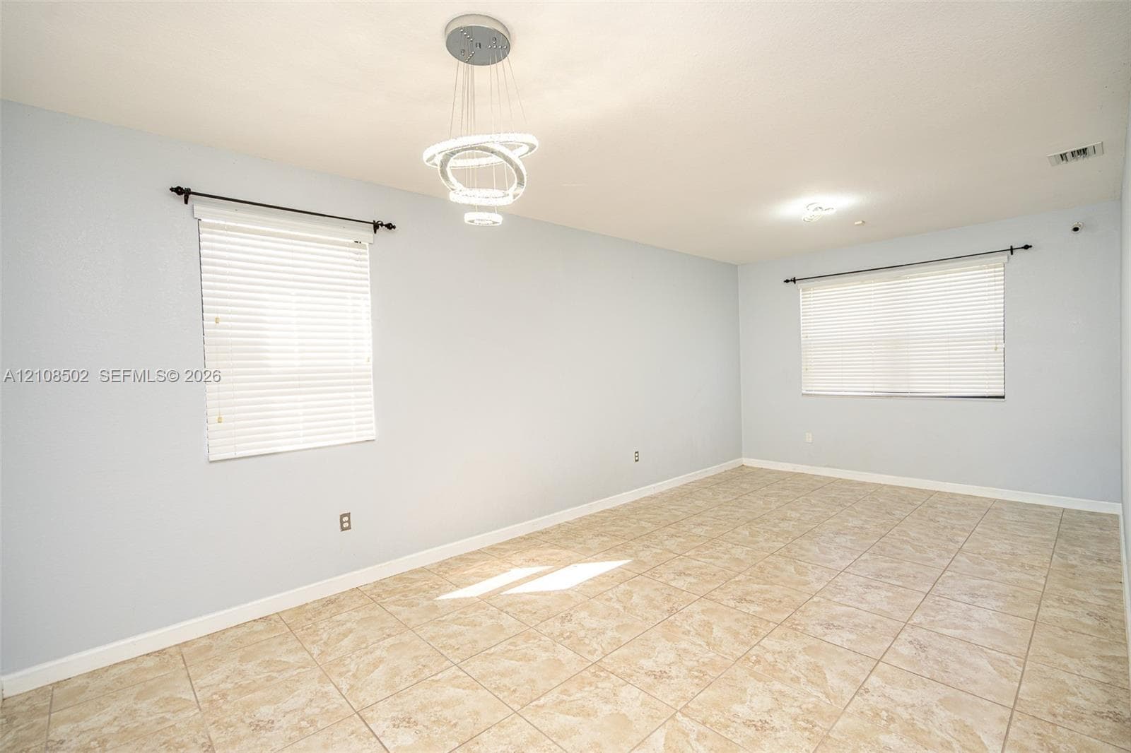 Interior space featuring ceramic tile flooring, neutral wall paint, modern multi-ring LED pendant lighting, and two windows with installed blinds
