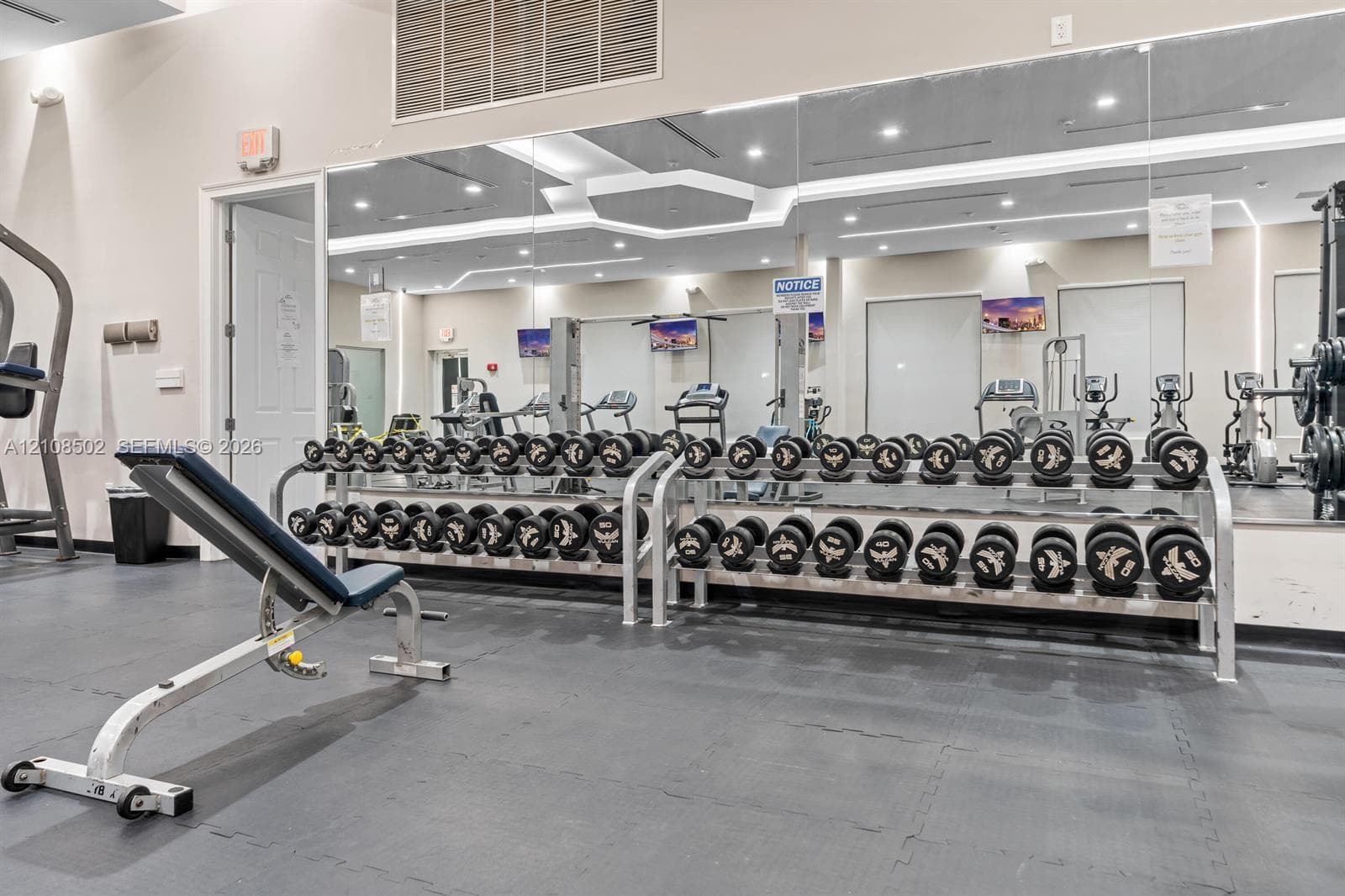 Fitness center featuring industrial-grade rubber flooring, wall-to-wall mirrors, and built-in metal dumbbell racks