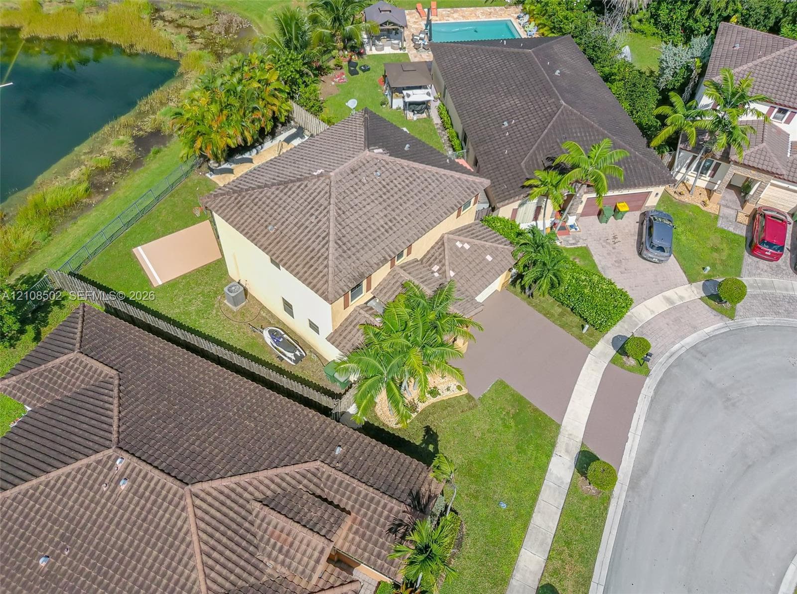 Aerial view of residential property featuring a tile roof, concrete driveway, and a backyard with an in-ground swimming pool overlooking a pond