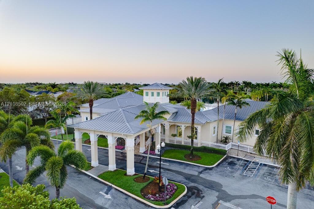 Stucco exterior building featuring a metal roof, prominent porte-cochere, central cupola, and surrounding landscaping