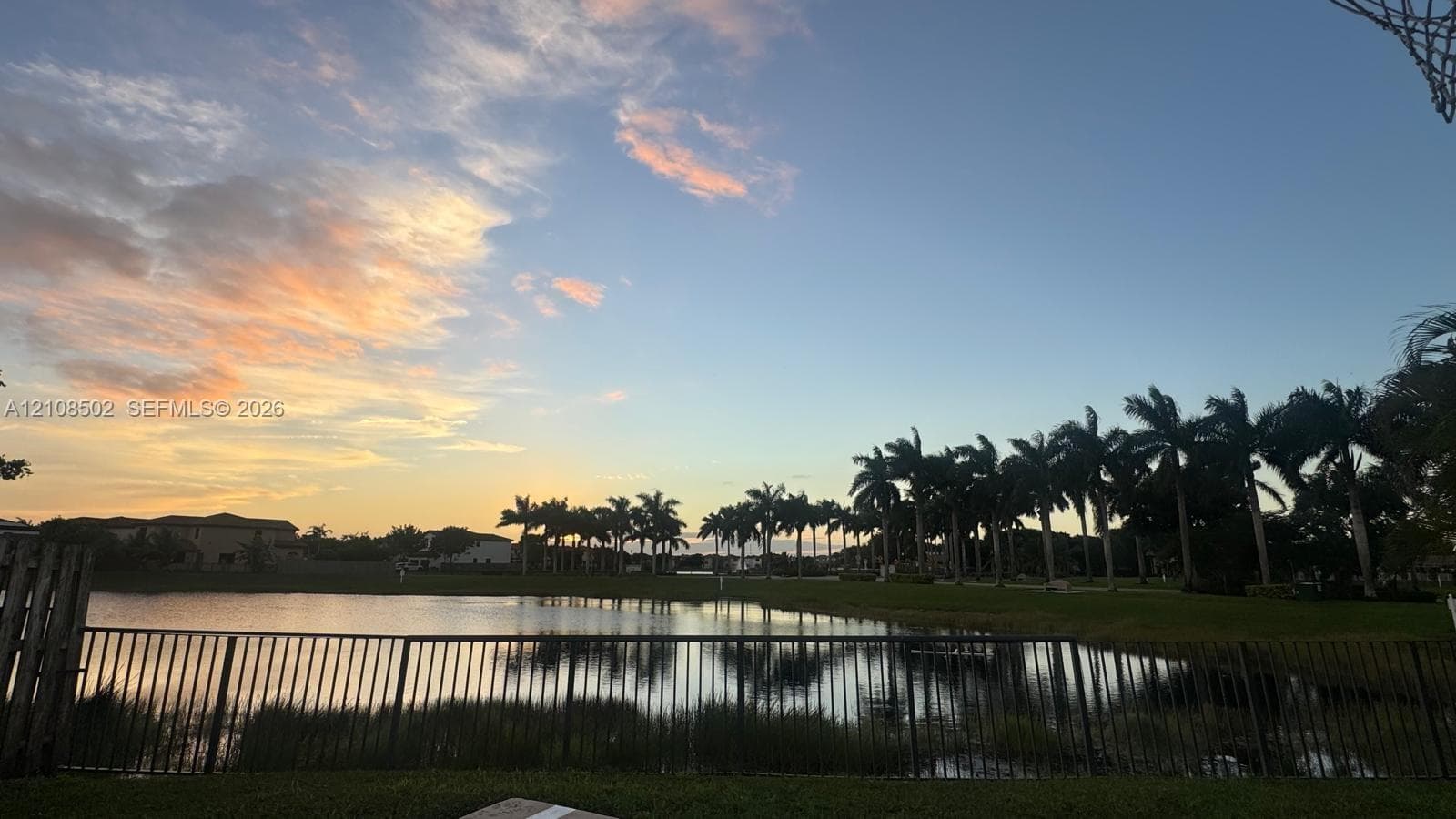Waterfront property featuring a metal perimeter fence, manicured lawn, and mature palm trees