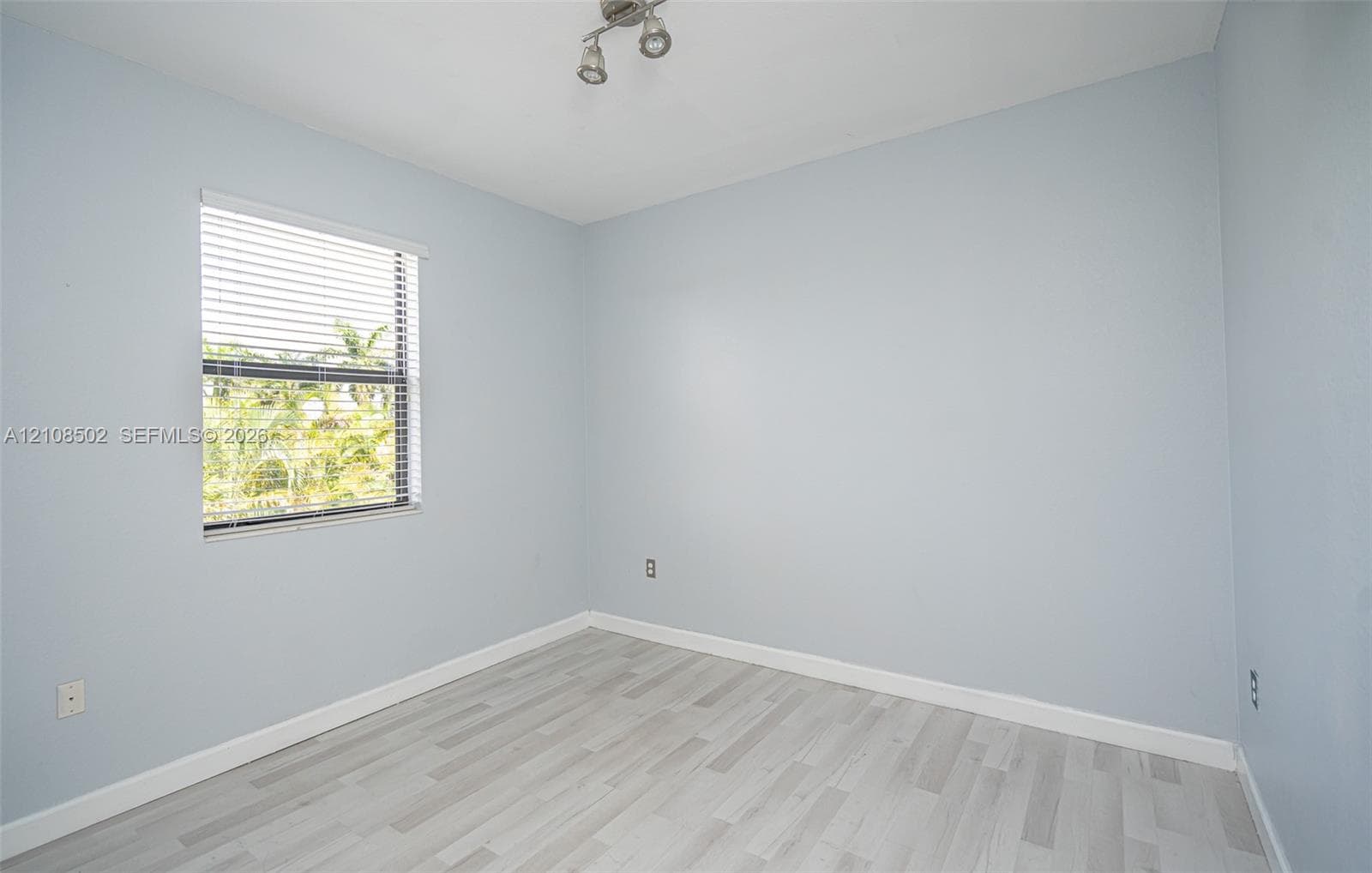 Neutral-toned interior featuring wood-finish flooring, a single window with horizontal blinds, and a multi-directional track light fixture