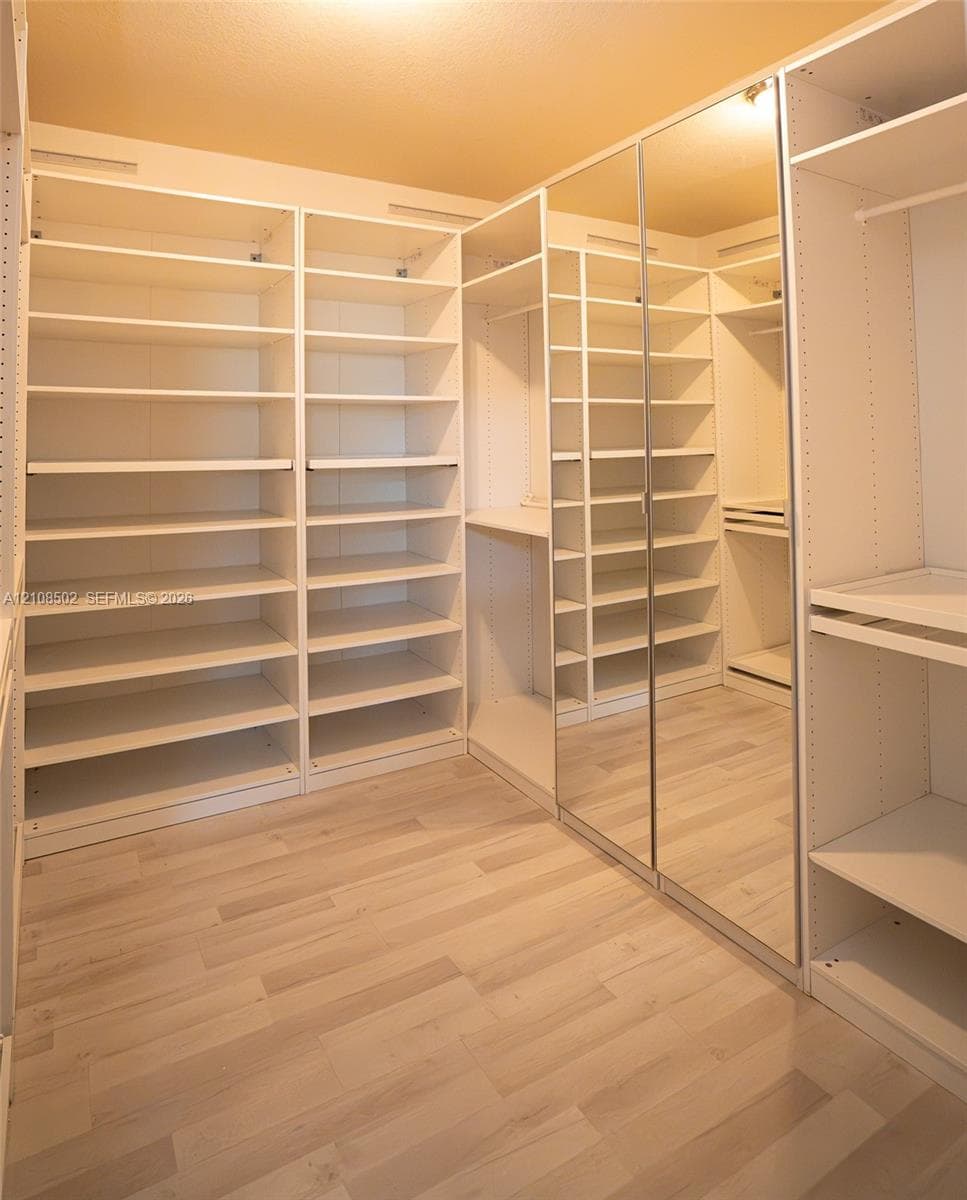 Walk-in closet featuring extensive built-in shelving, full-length mirrored door panels, wood-finish flooring, and integrated garment rods