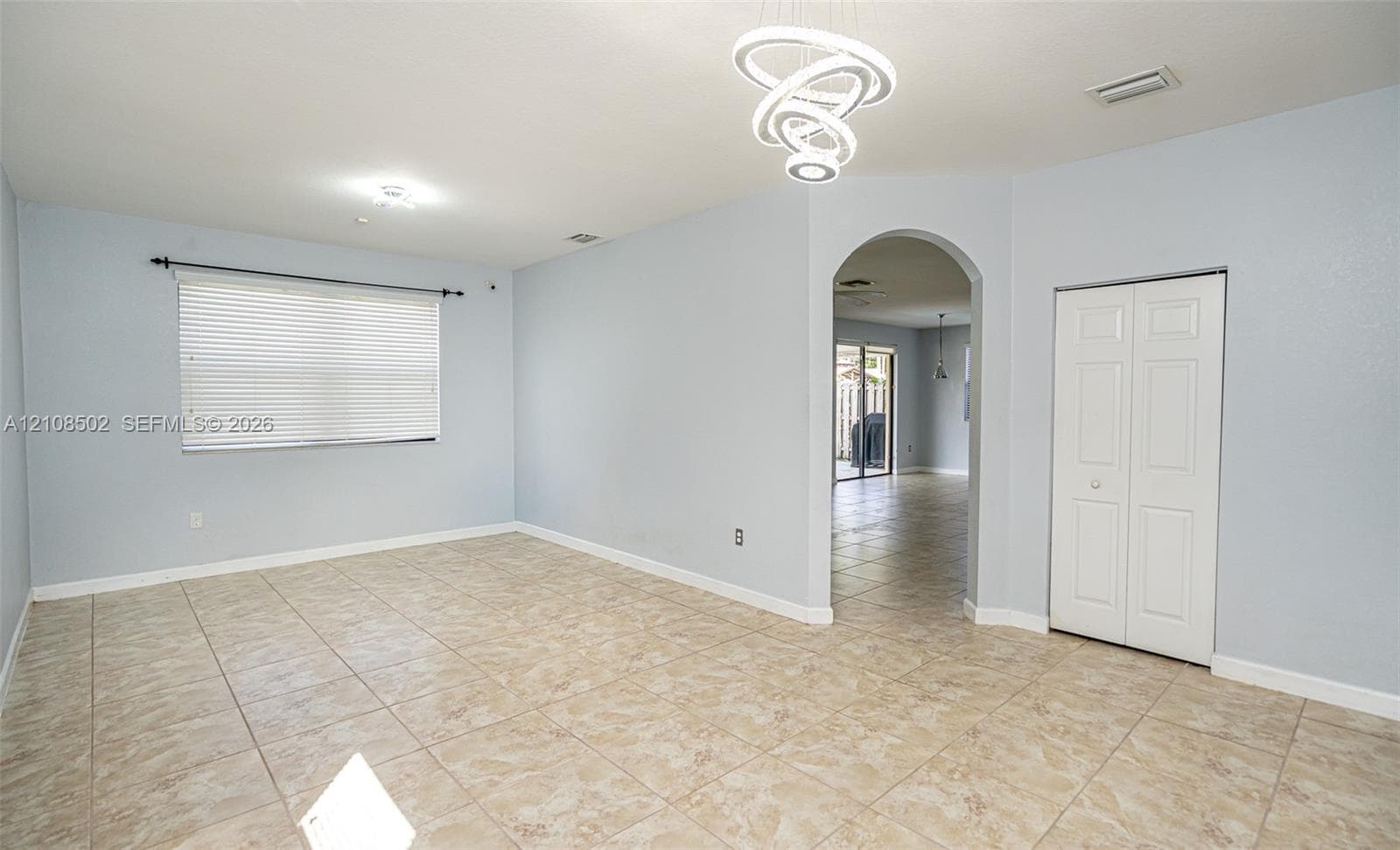 Interior space featuring tile flooring, modern sculptural LED chandelier, arched entryway, and double-door closet