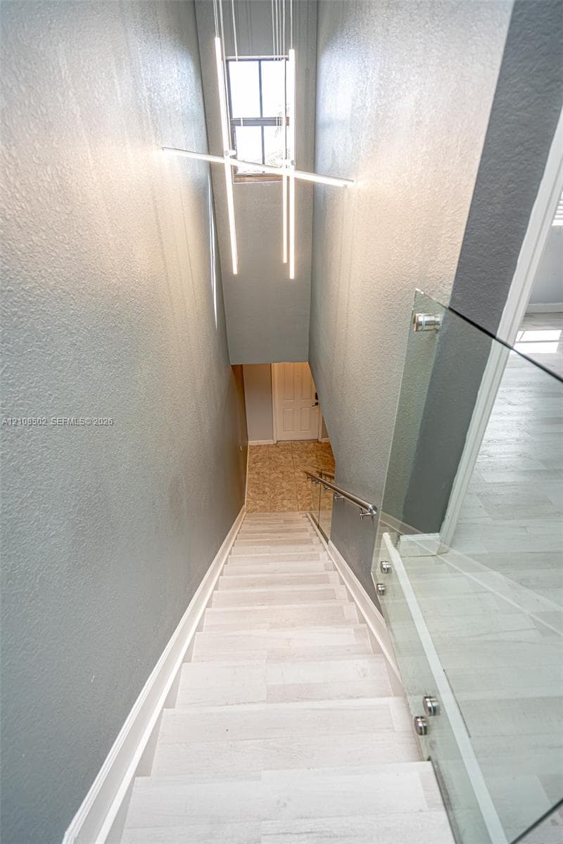 Staircase featuring wood-finish treads, glass panel railing with metallic hardware, and linear LED pendant lighting