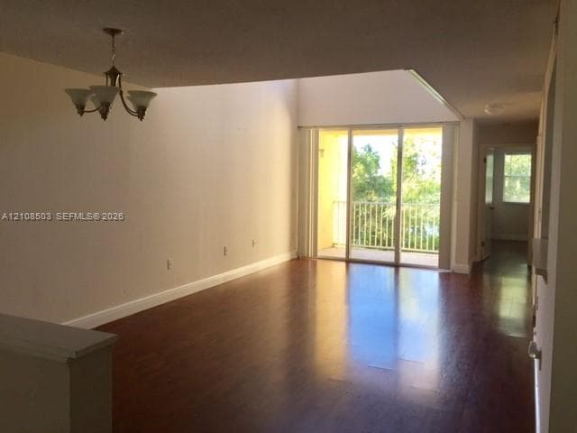 Living area featuring vaulted ceilings, wood-finish flooring, a multi-arm chandelier, and sliding glass doors opening to a private balcony