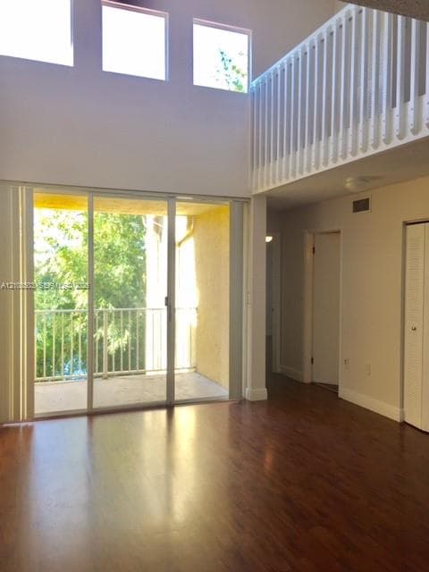 Double-height living area featuring wood-finish flooring, floor-to-ceiling sliding glass doors, upper-level interior balcony railing, and clerestory windows