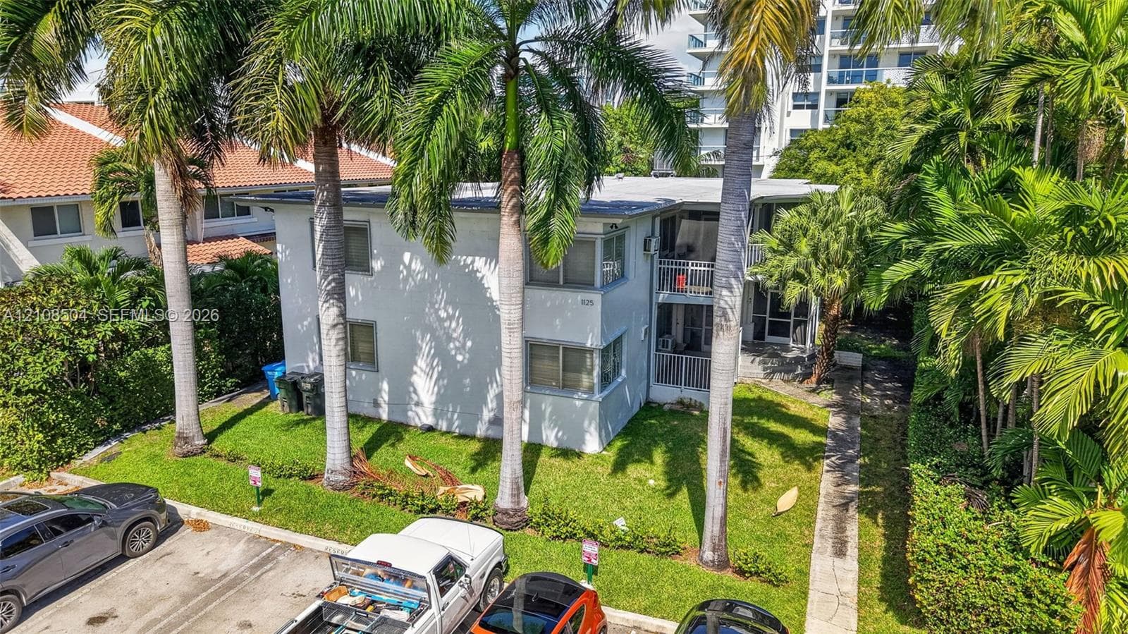 Two-story exterior featuring a light-toned smooth finish, multi-pane windows, and private railed balconies, situated on a lot with mature palm trees