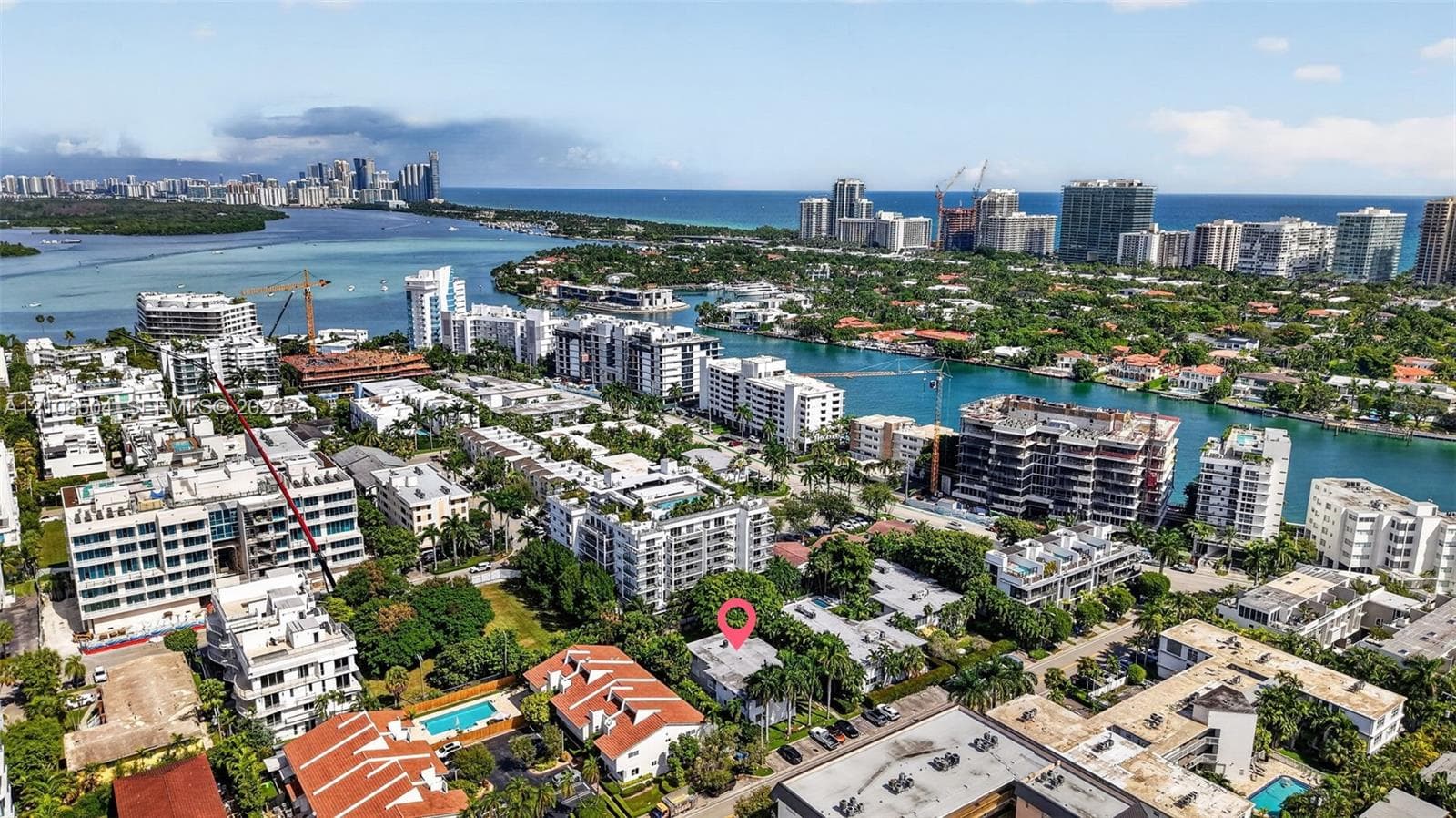 Aerial perspective of a coastal residential area featuring mature landscaping, proximity to waterfront channels, and urban skyline backdrops