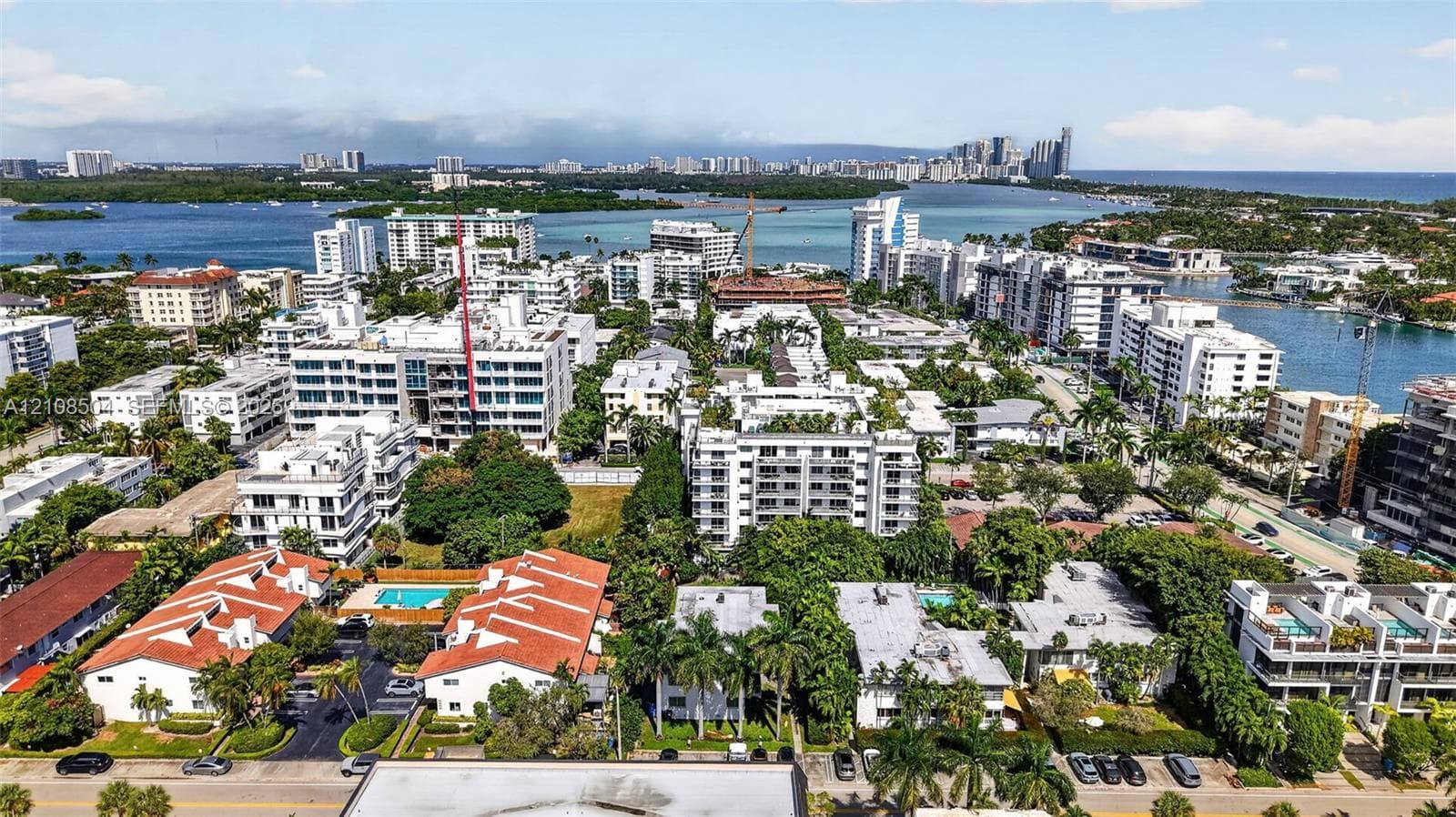 Aerial perspective of a coastal residential area featuring multi-level structures, terracotta-style roof tiles, established tropical landscaping, and proximity to expansive waterways