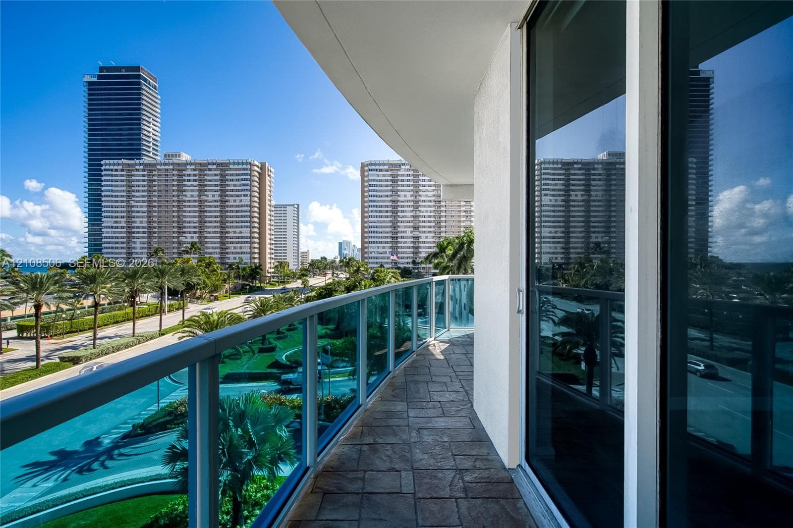 Private balcony featuring stone-patterned tile flooring, a sleek glass railing with metal framing, and full-height sliding glass doors