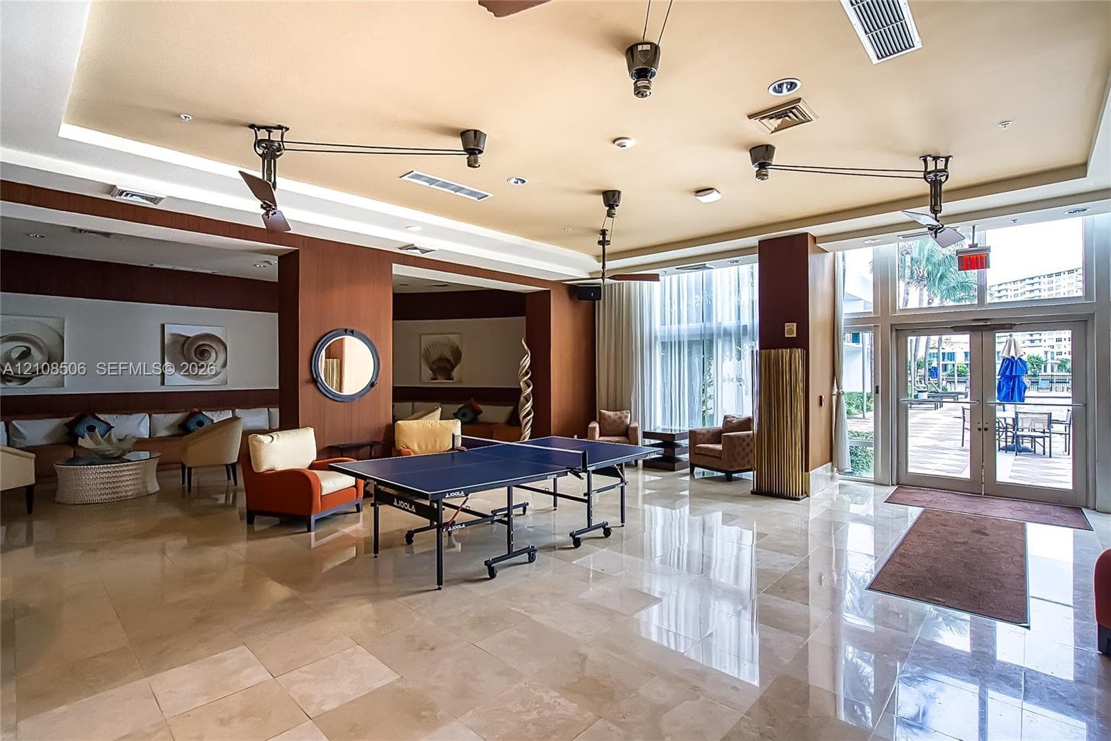 Common area featuring polished stone flooring, recessed ceiling tray detailing, wood-paneled walls, and expansive floor-to-ceiling glass panel doors