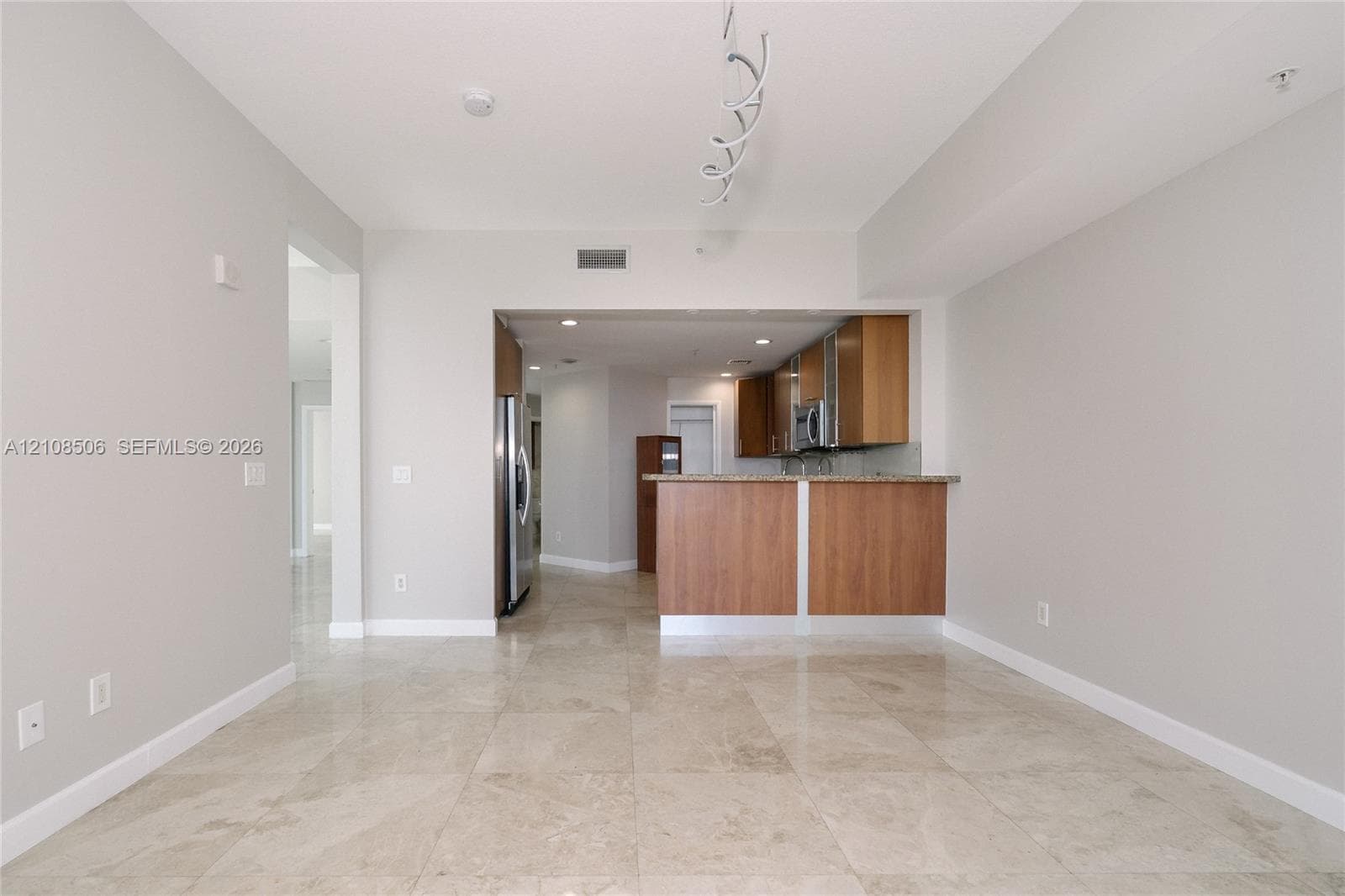 Open concept floor plan featuring light-toned tile flooring, wood-finish cabinetry, a peninsula breakfast bar, and stainless steel appliances