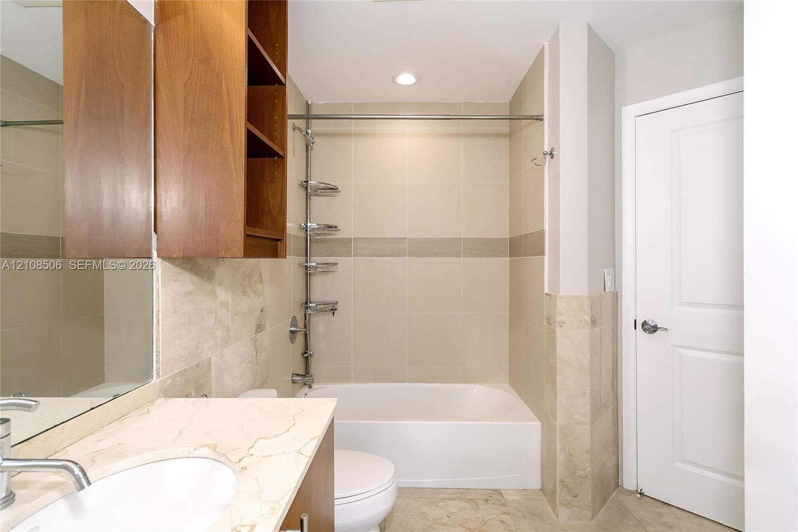 Bathroom featuring wood-finish cabinetry, stone-surface vanity countertop with an integrated basin, floor-to-ceiling tile surround, and built-in shelving