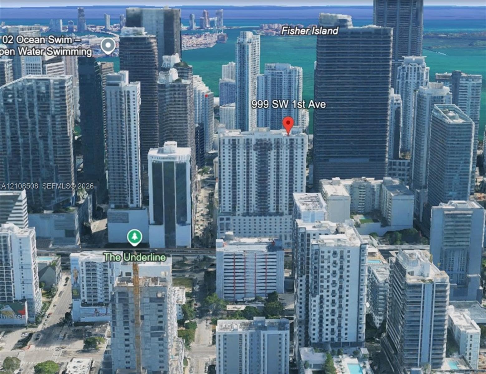 Aerial perspective of a high-rise residential building situated within a dense urban metropolitan center, featuring proximity to coastal waterways and developed city infrastructure