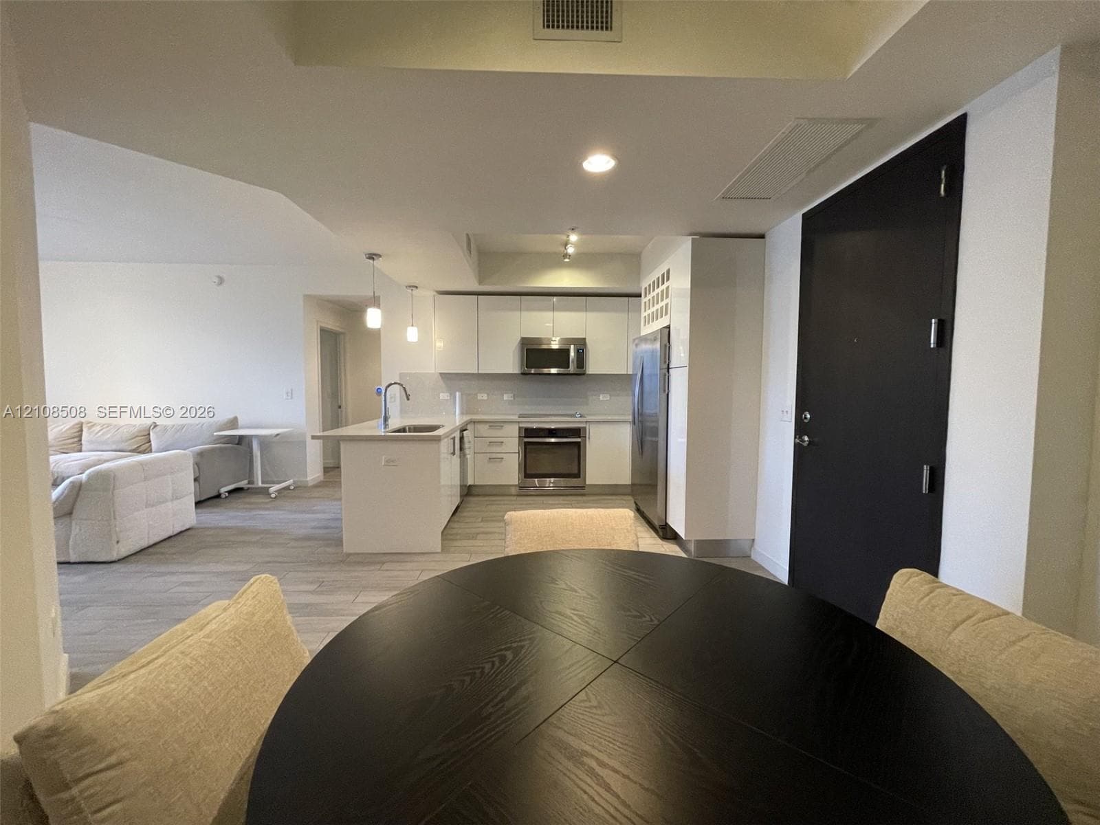 Modern kitchen featuring high-gloss white cabinetry, stainless steel appliances, a central island with a sink, and wood-finish flooring