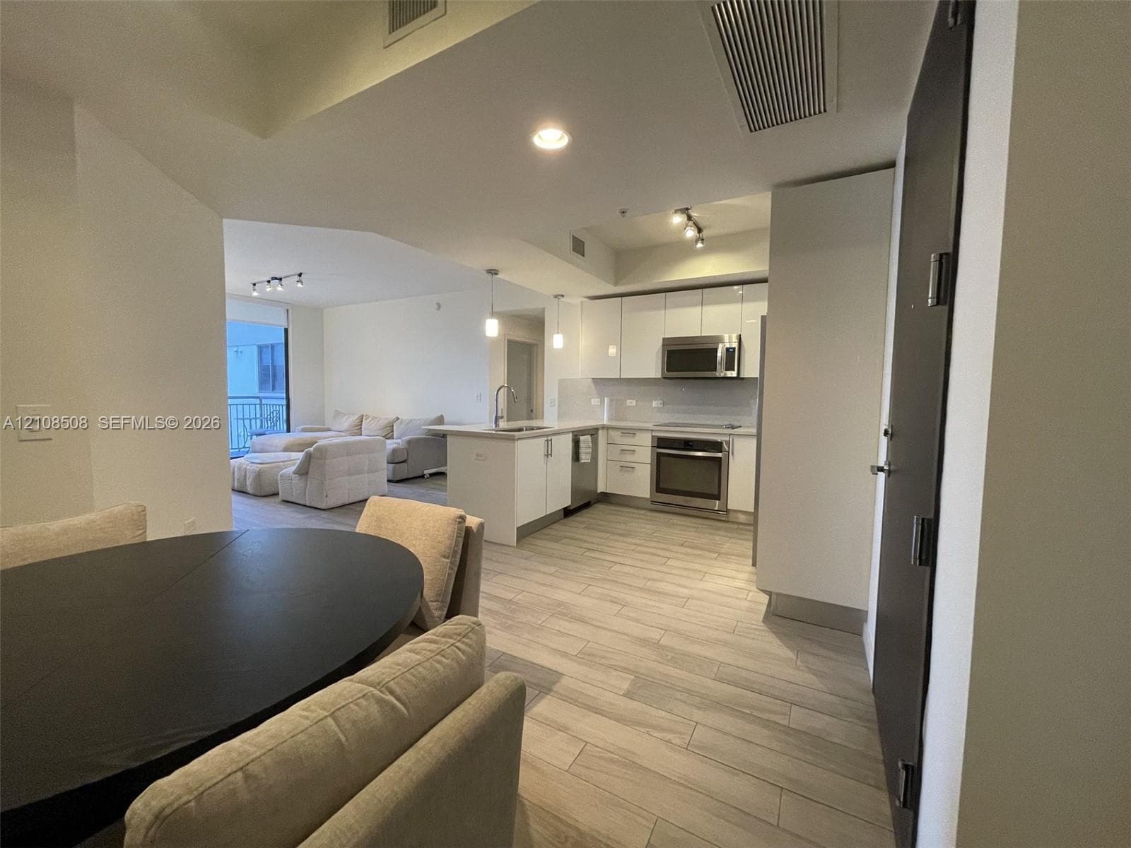 Kitchen featuring white flat-panel cabinetry, stainless steel appliances, stone countertops, and wood-finish flooring
