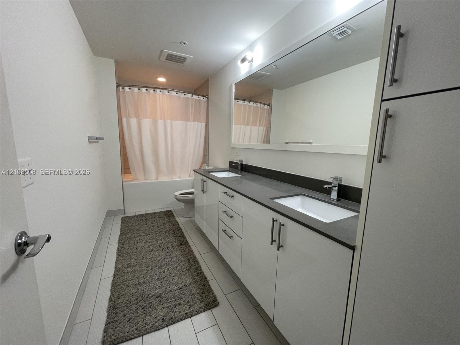 Bathroom featuring a double-sink vanity with white cabinetry, dark solid-surface countertops, a full-width mirror, and tile flooring