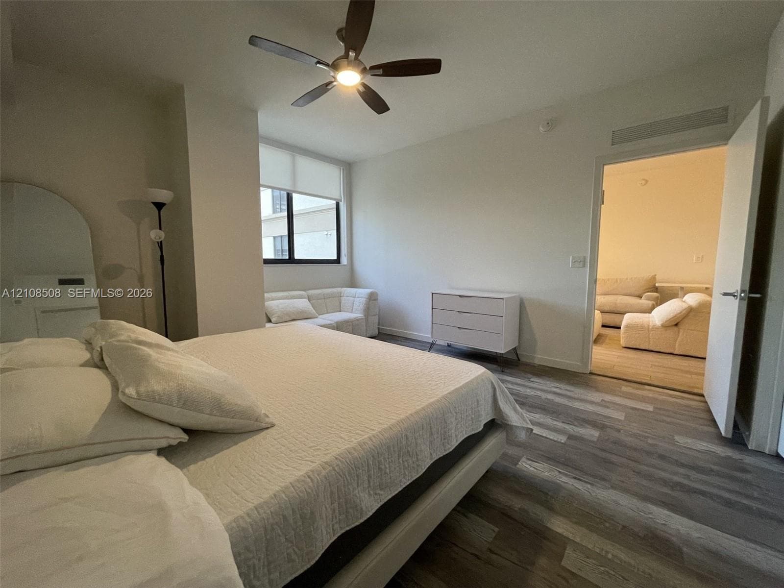Room featuring wood-finish flooring, a multi-blade ceiling fan with integrated lighting, and a window with a fitted roller shade