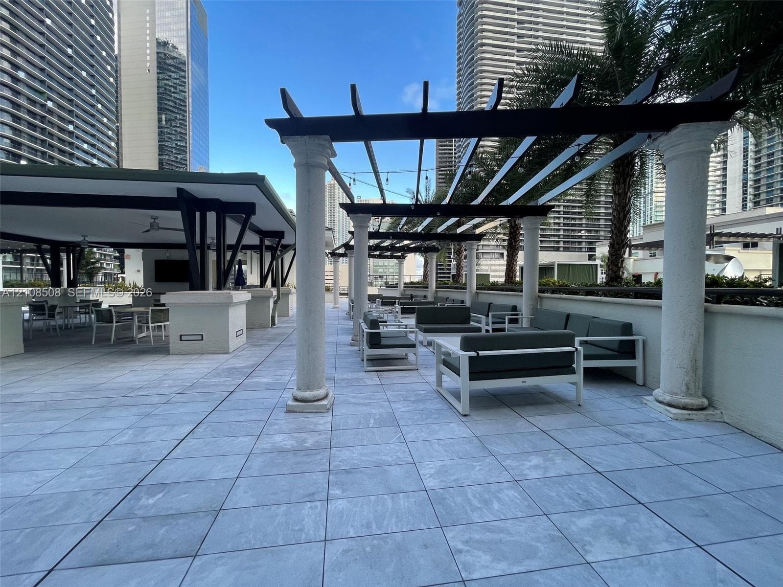 Outdoor terrace featuring stone-tiled flooring, pergola structures supported by architectural columns, a covered pavilion, and integrated wall-mounted lighting