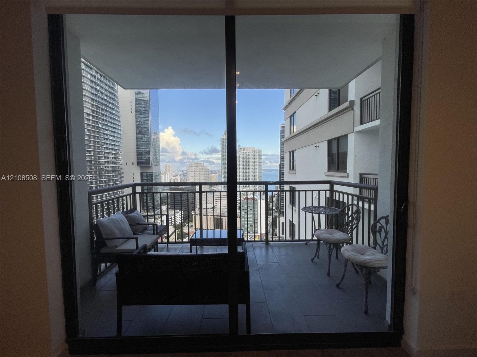 Covered balcony featuring tile flooring and metal railings, framed by floor-to-ceiling glass doors