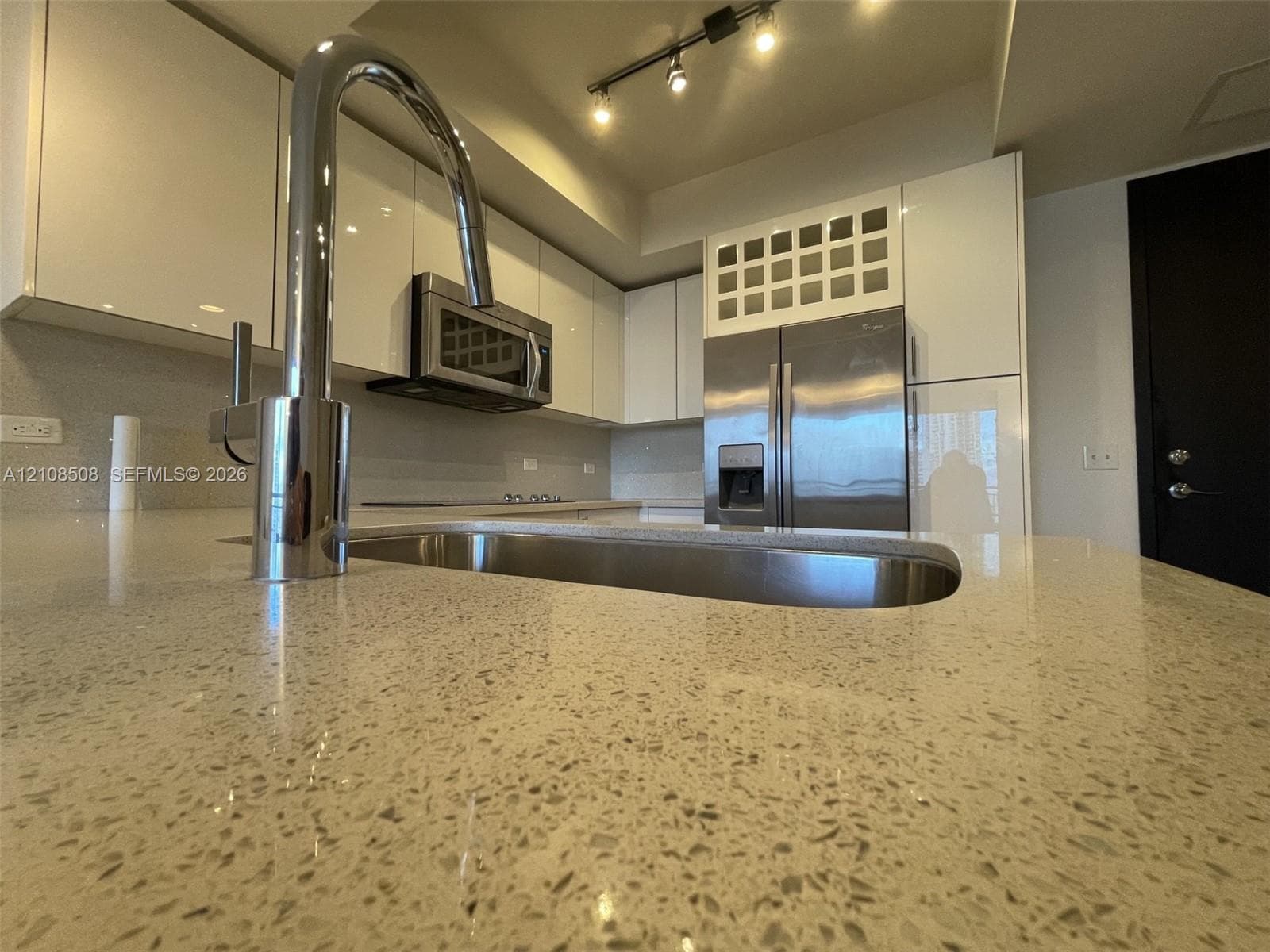 Kitchen featuring high-gloss cabinetry, stone countertops, stainless steel appliances, a high-arc faucet, and overhead track lighting