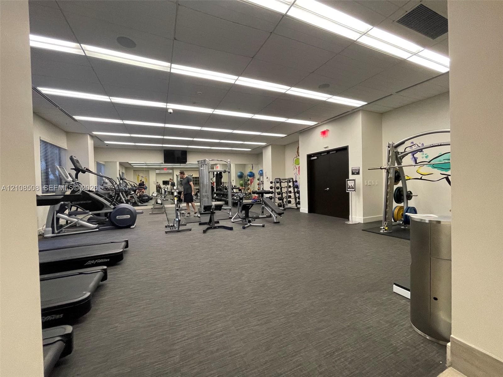 Fitness center featuring wall-to-wall mirrors, recessed linear lighting, and durable carpet flooring