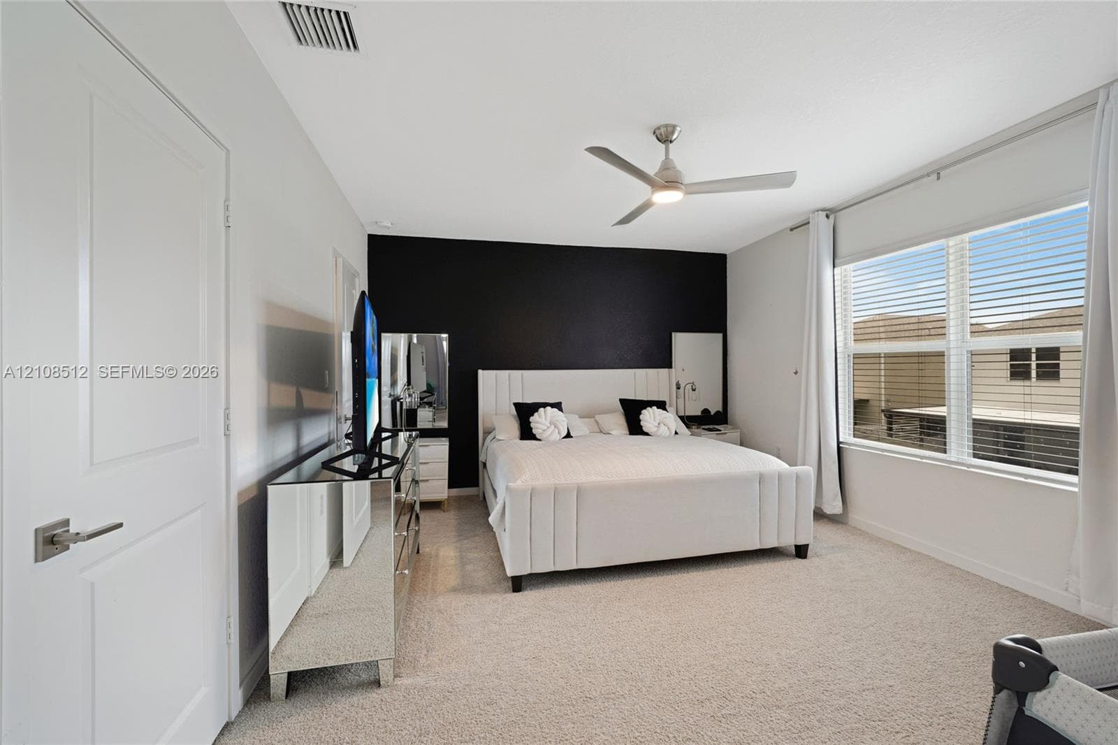 Bedroom featuring neutral carpeting, a high-contrast accent wall, and a multi-blade ceiling fan with integrated lighting