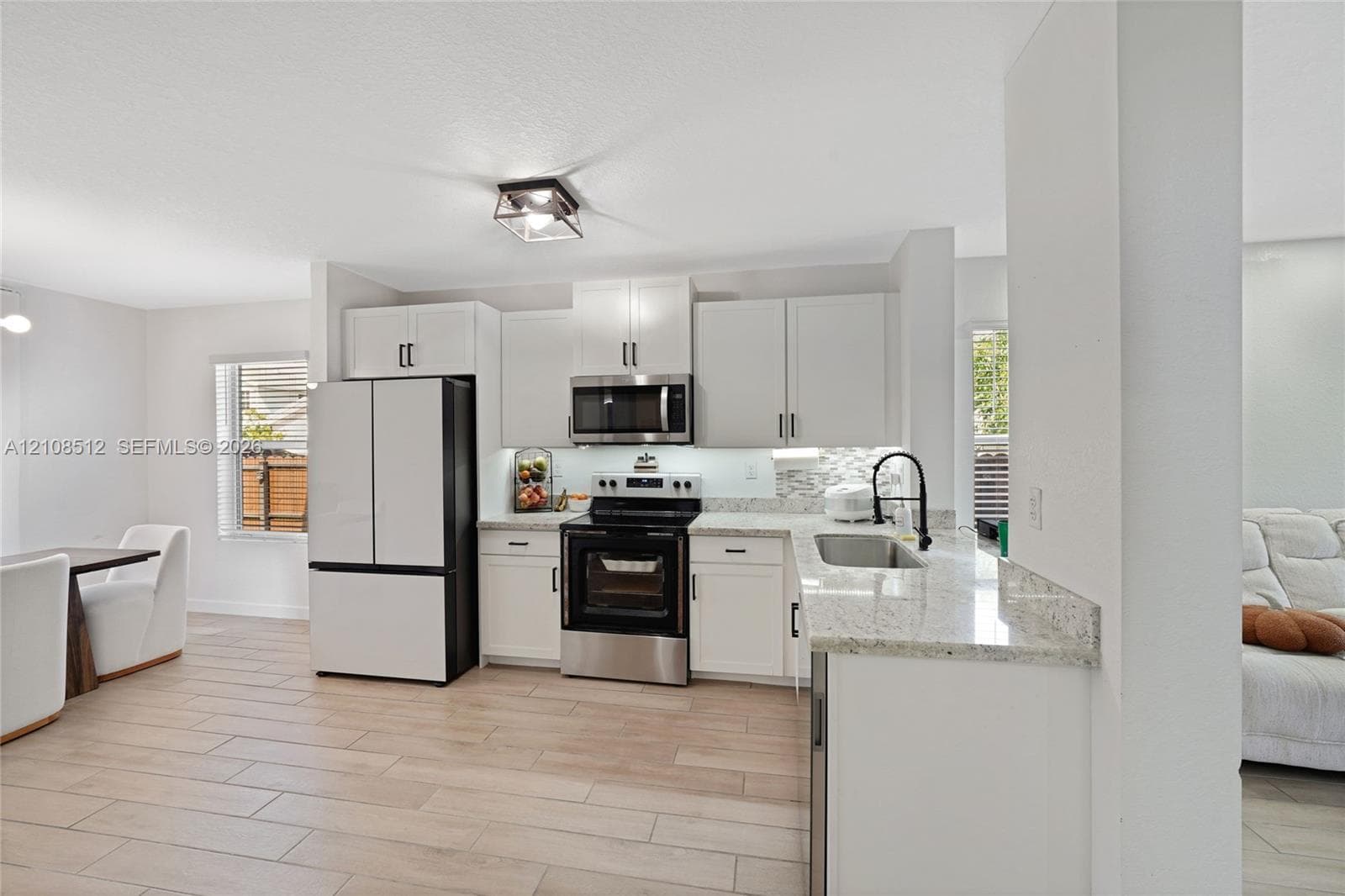 Kitchen featuring white cabinetry, stone-finish countertops, stainless steel appliances, a high-arc faucet, and wood-finish flooring