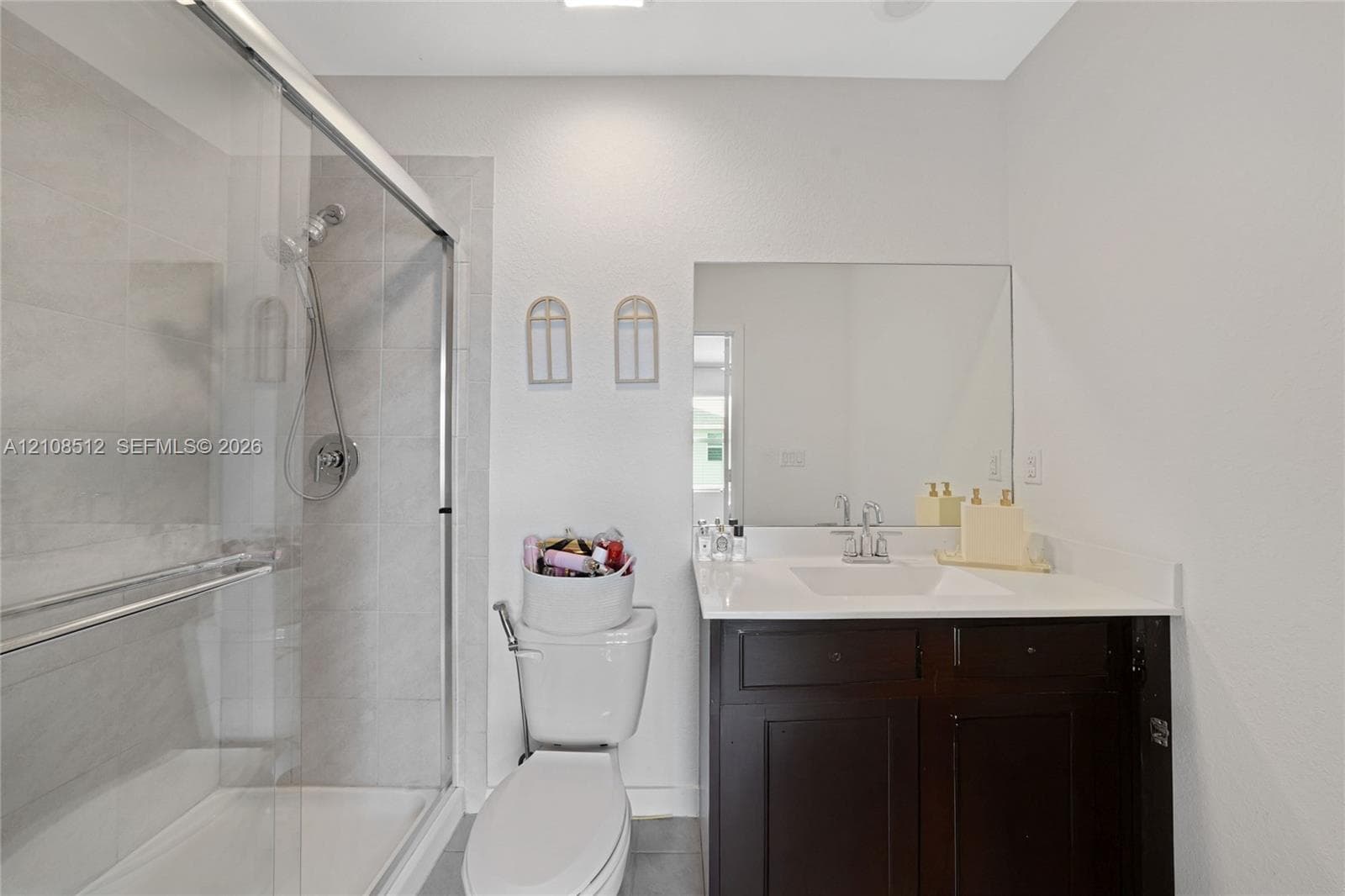 Bathroom featuring a dark wood-finish vanity with a stone countertop, an integrated rectangular sink, a glass-enclosed shower with tiled surround, and a large wall-mounted mirror