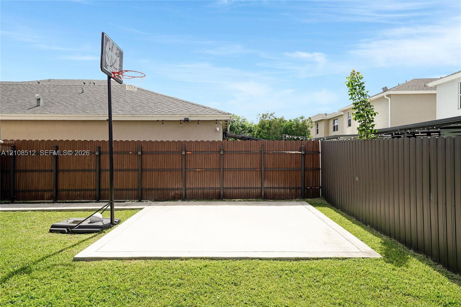 Private backyard featuring a concrete sport court, perimeter wood privacy fencing, and metal panel fencing