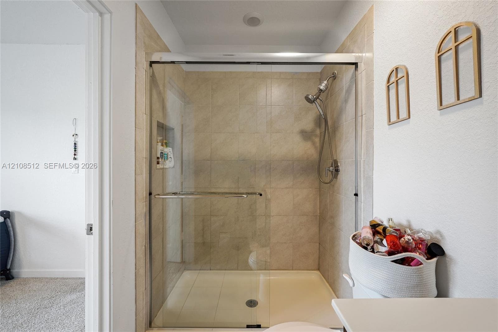 Shower enclosure featuring floor-to-ceiling neutral tile, a built-in recessed storage niche, a sliding glass door system, and a handheld shower fixture