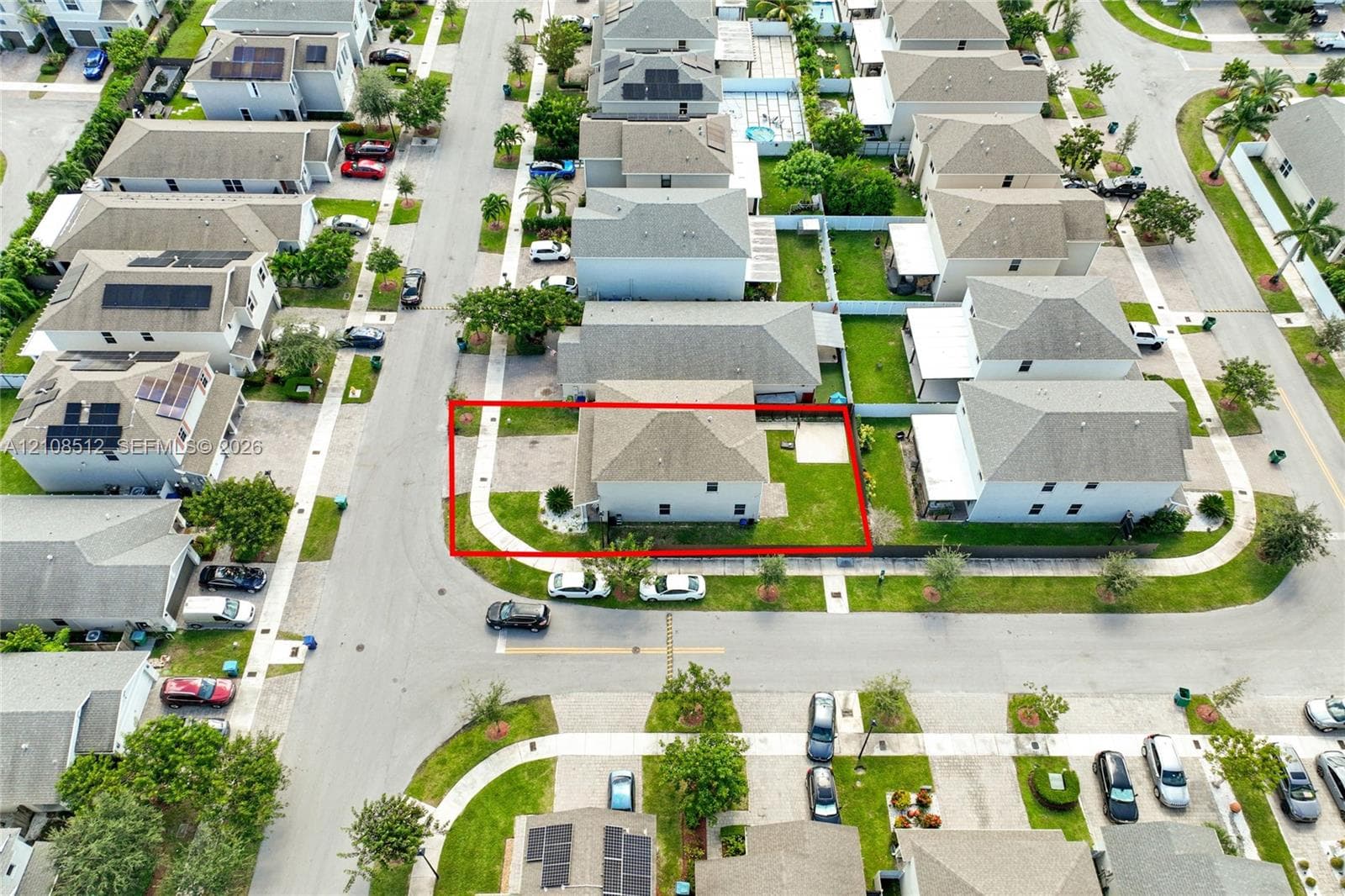 Aerial view of a corner lot property featuring a hip roof, exterior concrete walkway, paved ground-level patio, and lawn space