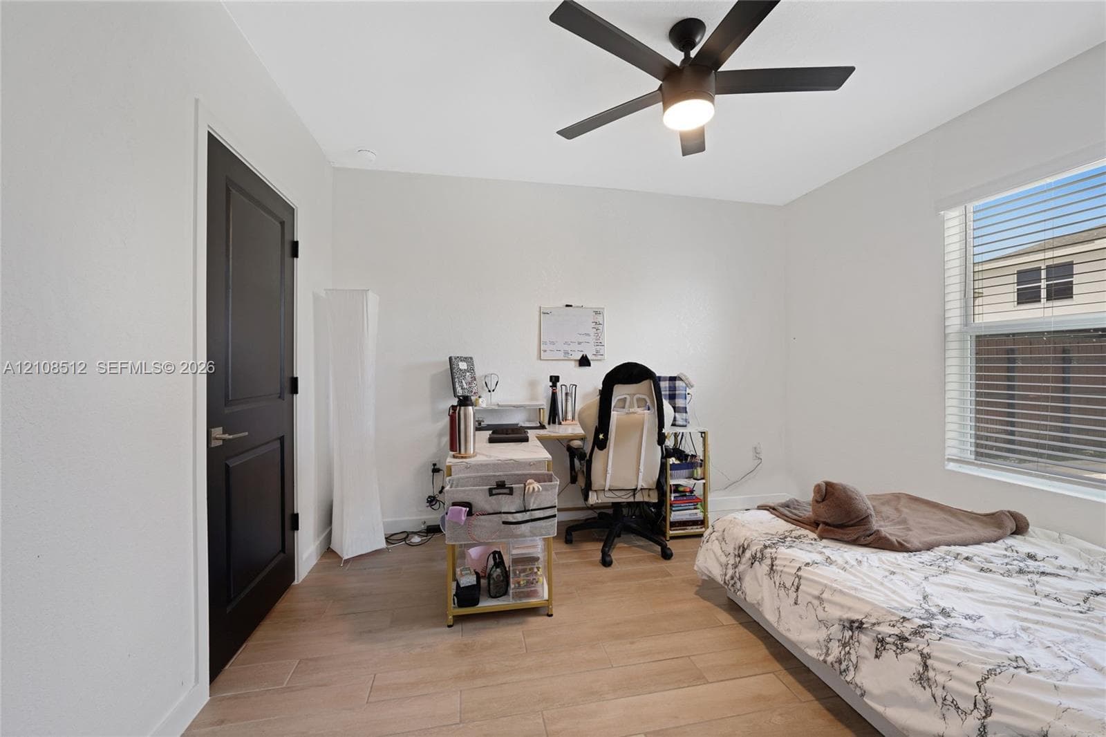 Interior room featuring wood-finish flooring, a matte black door, a matte black ceiling fan with integrated lighting, and window blinds