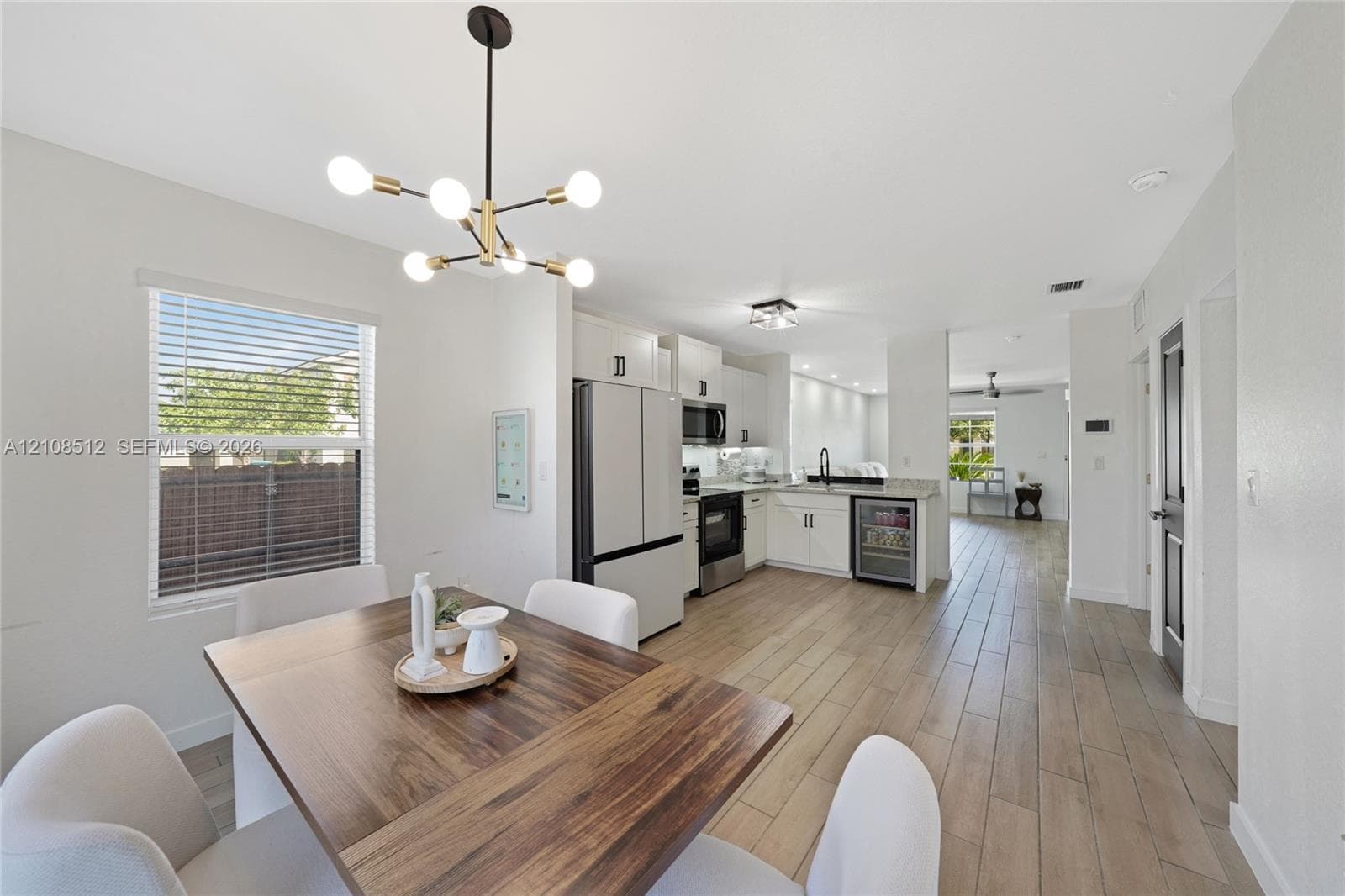 Kitchen featuring white cabinetry, wood-finish flooring, stainless steel appliances, a beverage refrigerator, and a multi-arm geometric chandelier