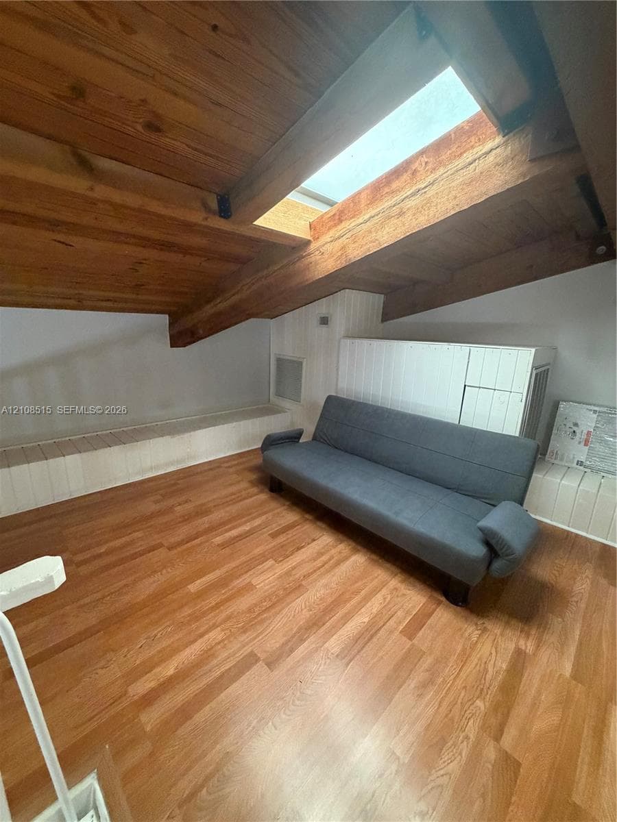 Vaulted ceiling featuring exposed wood beams, skylight, wood-finish flooring, and built-in wall cabinetry