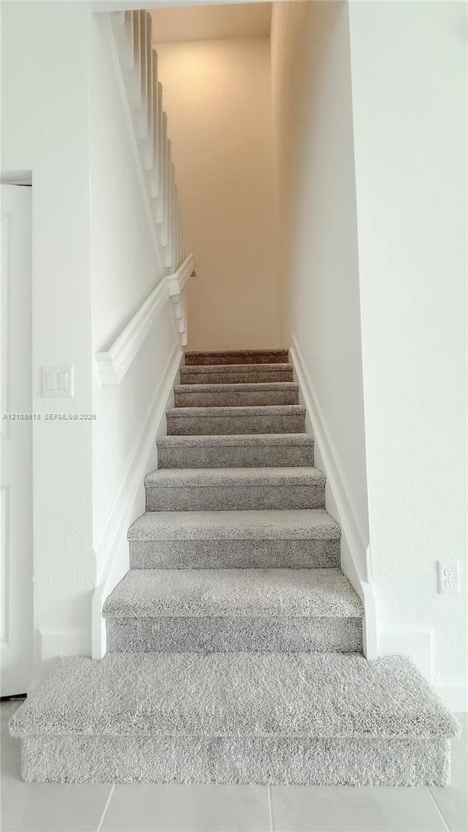 Staircase featuring neutral-tone carpeting, white painted wooden handrails, and white millwork