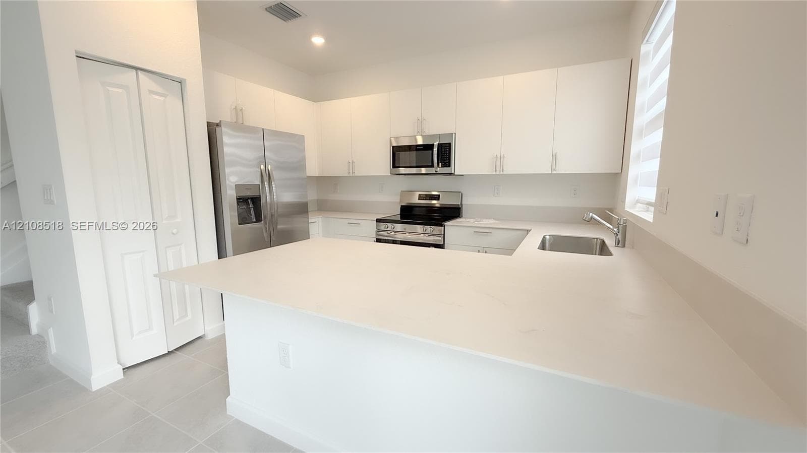 Kitchen featuring white flat-panel cabinetry, quartz countertops, stainless steel appliances, and a peninsula with an integrated sink