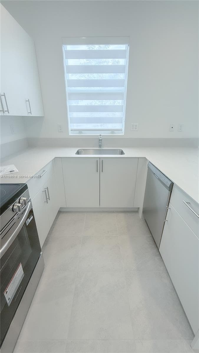 Kitchen featuring white flat-panel cabinetry, light-toned stone-finish countertops, stainless steel appliances, a stainless steel undermount sink, and tile flooring