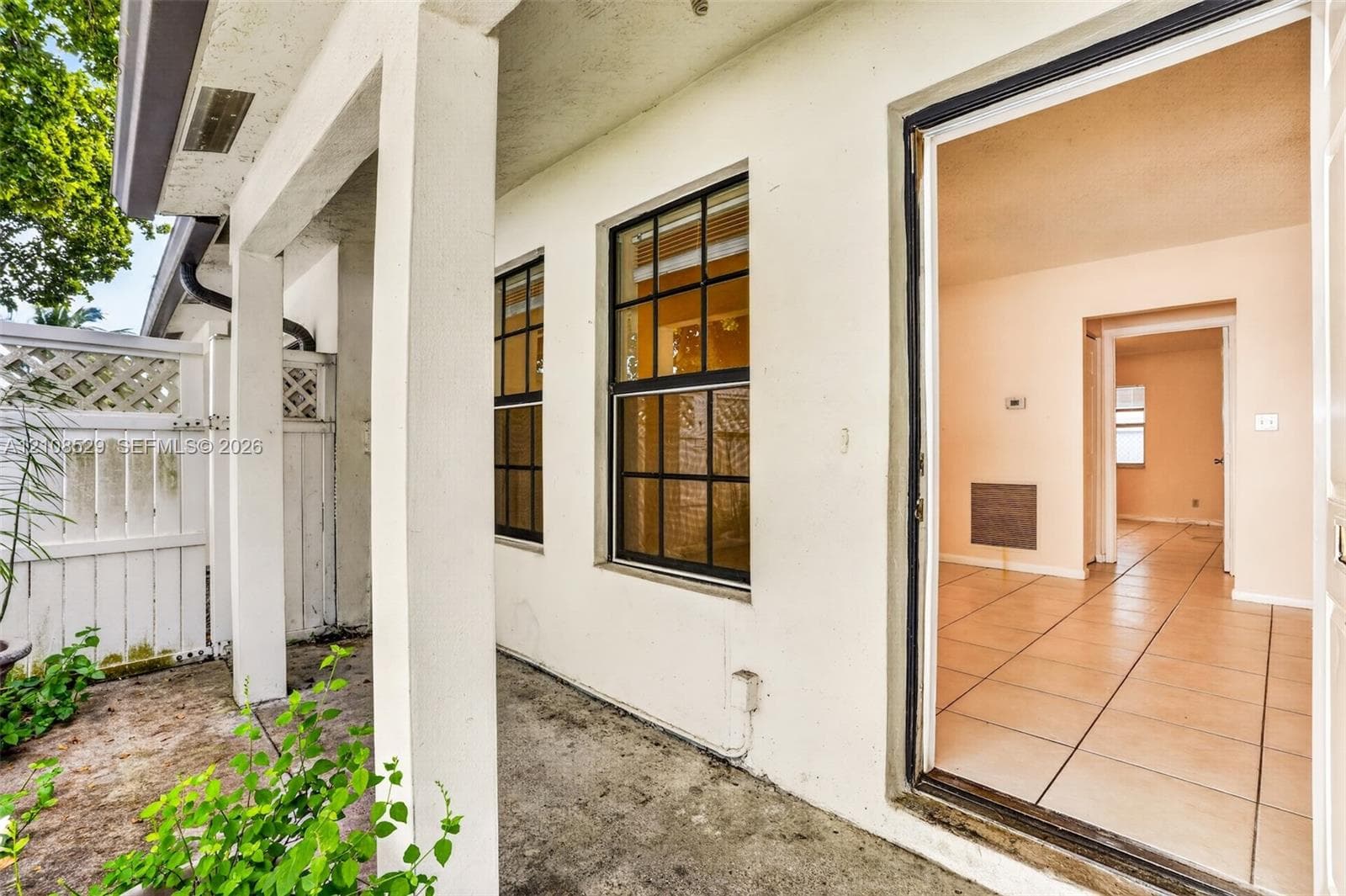 Covered patio featuring concrete flooring, white lattice privacy fencing, multi-pane windows with dark frames, and ceramic tile flooring throughout the interior