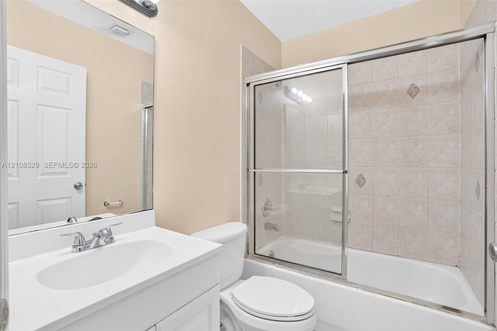Bathroom featuring a white vanity cabinet, solid-surface countertop with an integrated sink, polished chrome faucet, and a shower-tub combination with sliding glass doors and tiled surround