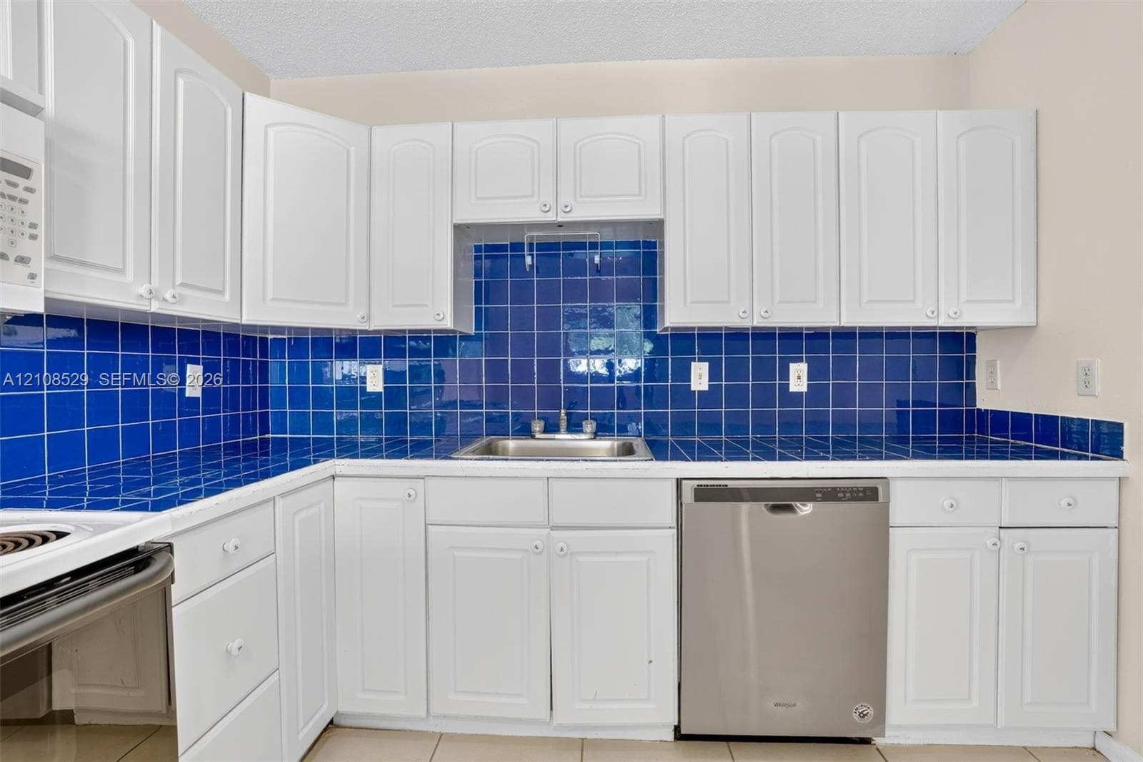 Kitchen featuring white shaker-style cabinetry, a deep blue tiled backsplash, coordinating tile countertops, and a stainless steel dishwasher