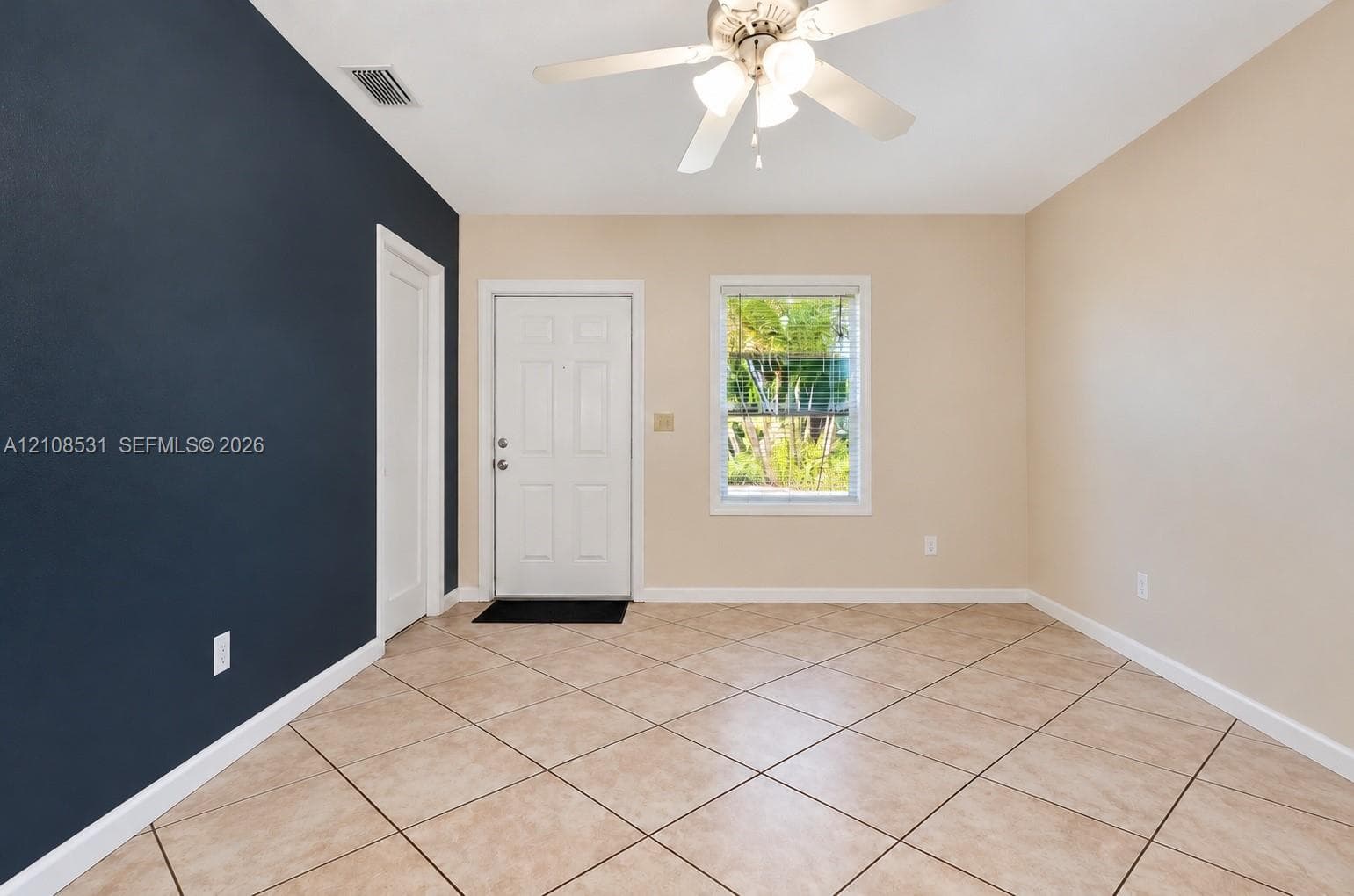 Room featuring diagonal tile flooring, a dark accent wall, a solid entry door, and a ceiling-mounted light fixture with integrated fan