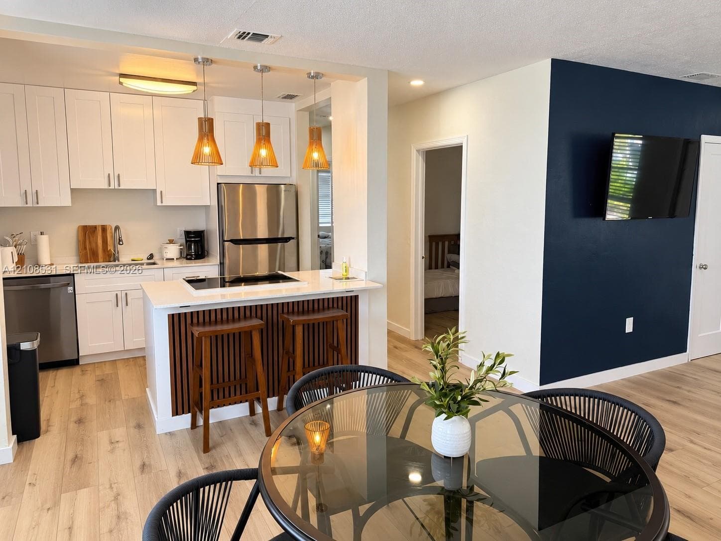 Kitchen featuring white cabinetry, quartz-surface countertops, stainless steel appliances, and a wood-slat breakfast bar accented by hanging pendant lighting