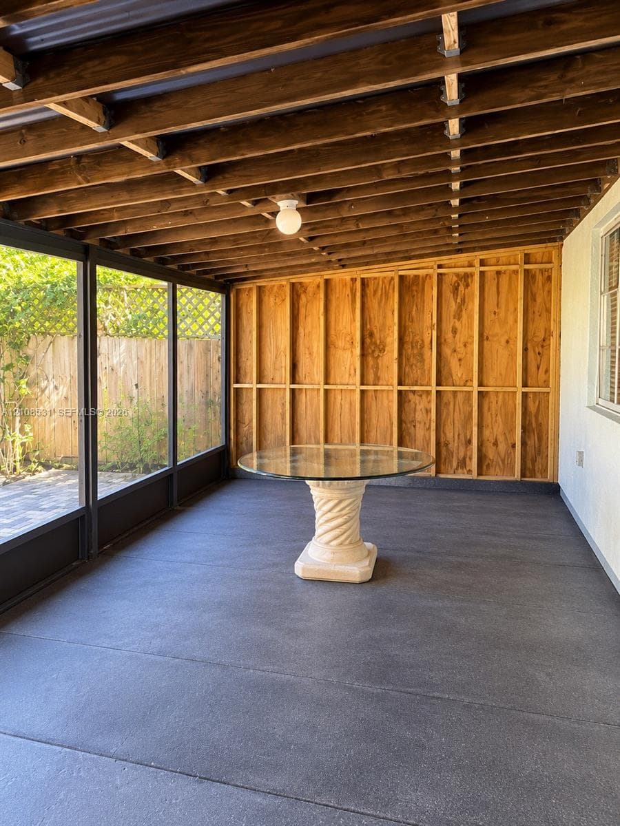 Enclosed porch featuring an exposed wood-beam ceiling, concrete flooring, and screen wall panels