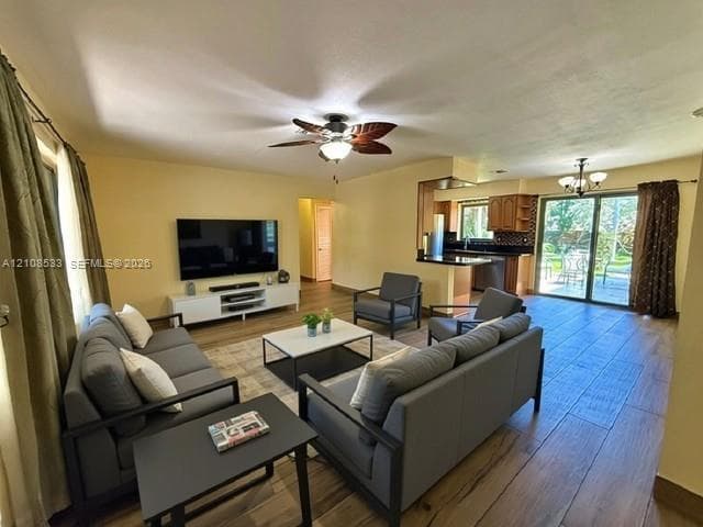 Open floor plan featuring wood-finish flooring, ceiling fan with light fixture, kitchen with cabinetry and dark countertops, and sliding glass doors