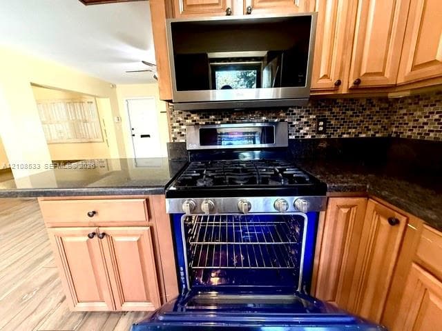 Kitchen featuring stained wood cabinetry, stone countertops, stainless steel gas range with convection oven, built-in microwave, and mosaic tile backsplash