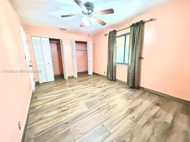 Wood-finish flooring, dual closets with louvered doors, and a ceiling-mounted light fixture with fan