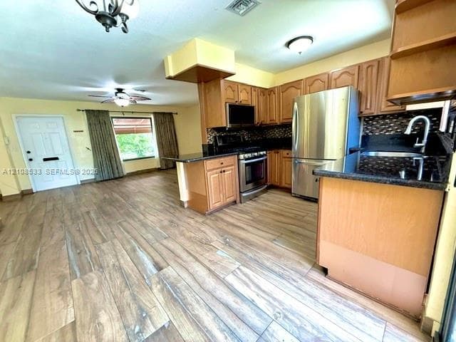 Kitchen featuring wood-finish flooring, stainless steel appliances, dark stone-composite countertops, and wood cabinetry