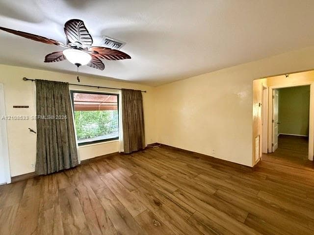 Room interior featuring wood-finish flooring, a decorative leaf-blade ceiling fan, and a large window